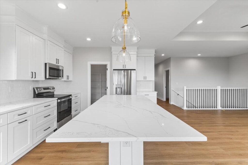 Modern kitchen featuring white cabinets and a marble island, showcasing new Gladiator Homes for sale in Norwalk, IA.