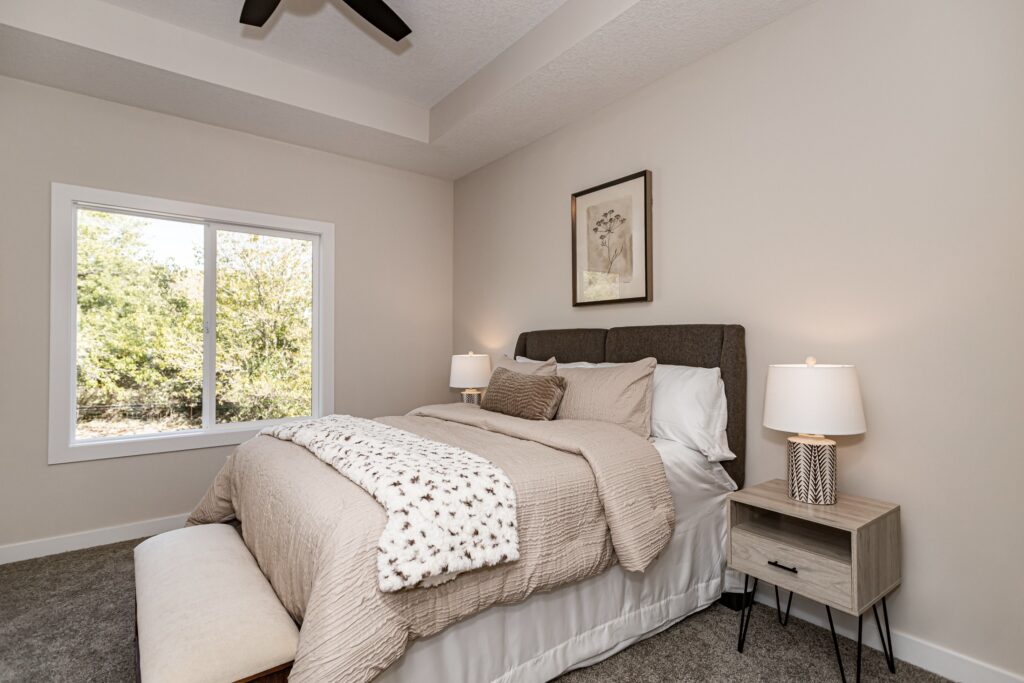 A well-furnished bedroom with a bed, nightstand, and window, part of Gladiator Homes for sale at 5825 Westfield Dr, Ames, IA.