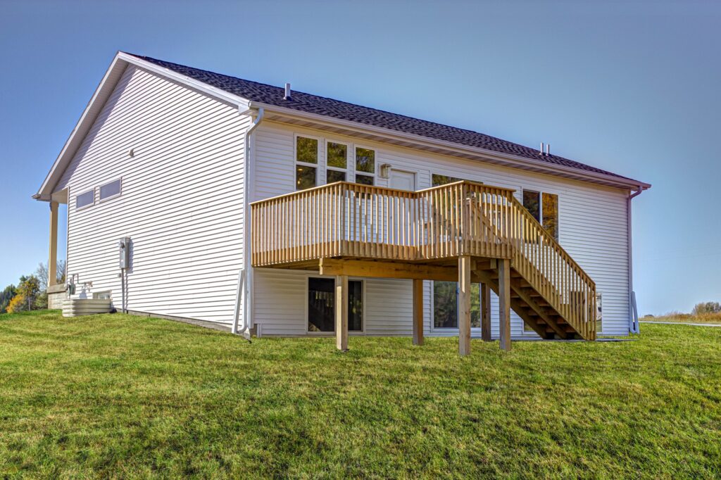 A modern two-story house with a wooden deck and large windows, surrounded by a well-manicured lawn under a clear blue sky loccated at 5825 Westfield Dr, Ames, IA