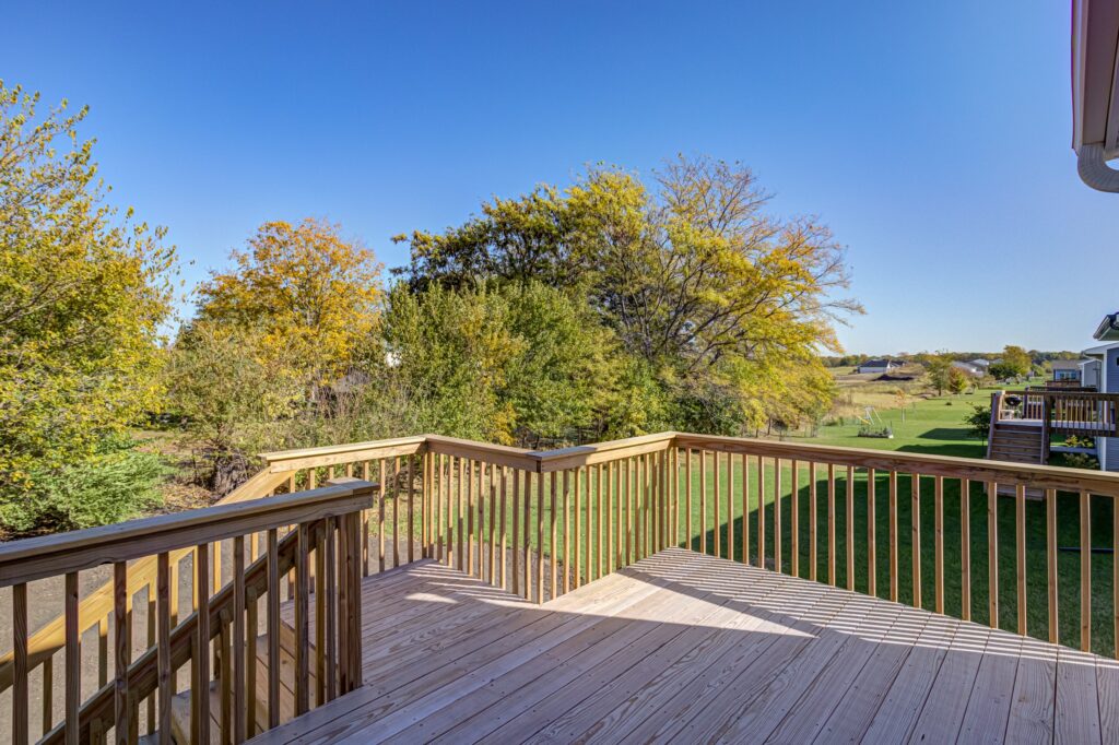 A wooden deck with a railing offers a view of trees, highlighting the outdoor area of a home for sale at 5825 Westfield Dr, Ames, IA.