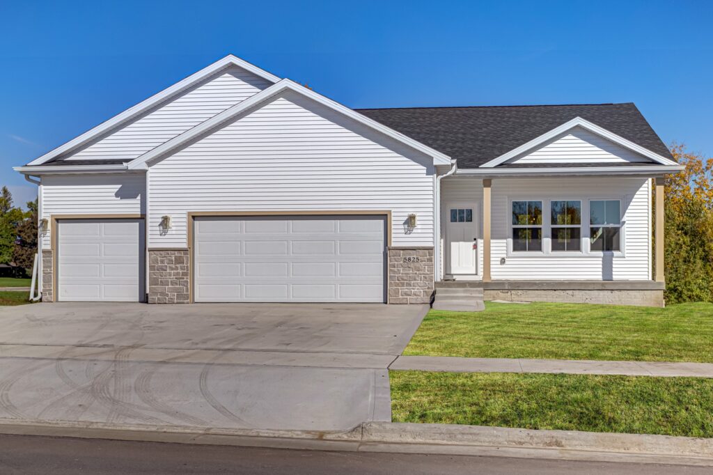 A modern single-story house with a white exterior, three garage doors, and a neat front lawn under a clear blue sky.