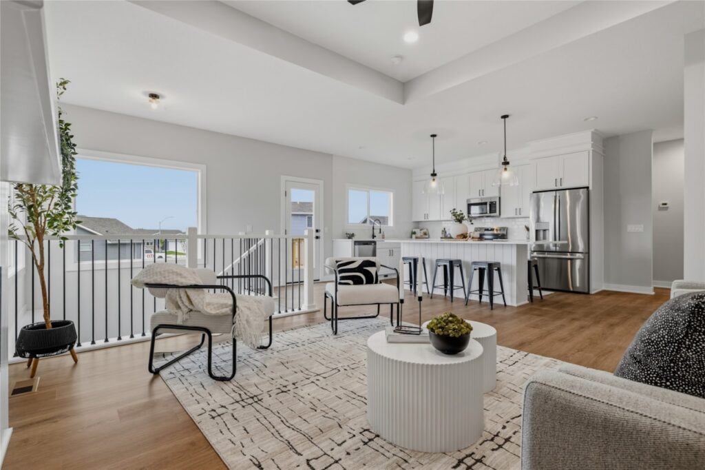 Bright living room open to kitchen with tray ceiling, black staircase railing, and large windows in Waukee Iowa new construction