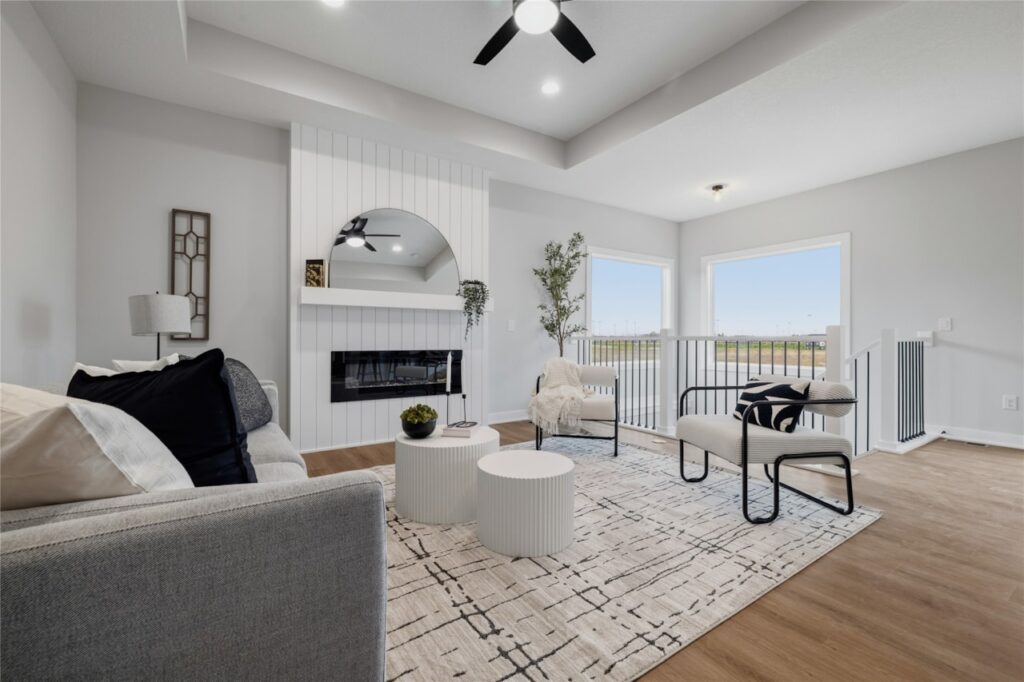 Living room with shiplap fireplace, arched mirror, tray ceiling, and open black iron railing in Waukee Iowa new home