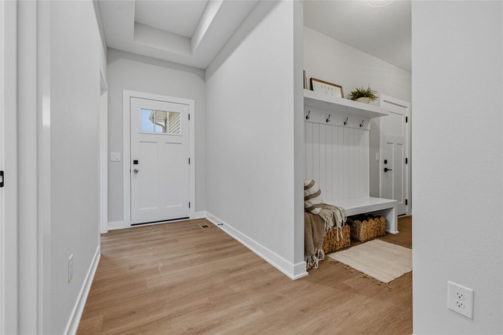 Entry hallway with craftsman front door, tray ceiling, and mudroom nook with bench and coat hooks in Waukee Iowa new build