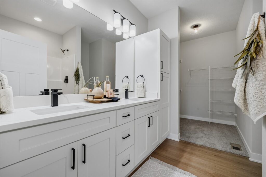 Primary bathroom with double white shaker vanity, quartz countertop, matte black hardware, and walk-in closet in Waukee Iowa new build