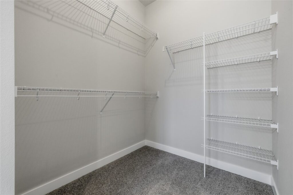 Primary walk-in closet with white wire shelving, hanging rods, and carpet in Waukee Iowa new construction home
