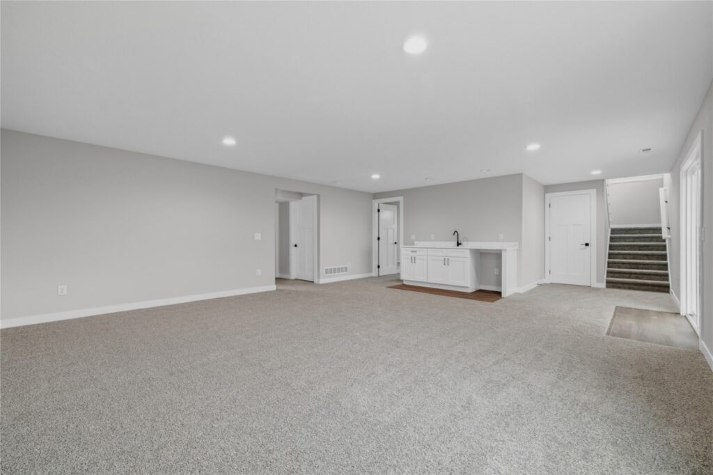 Large finished lower level rec room with carpet, recessed lighting, wet bar, and door to bedroom in Waukee Iowa new construction