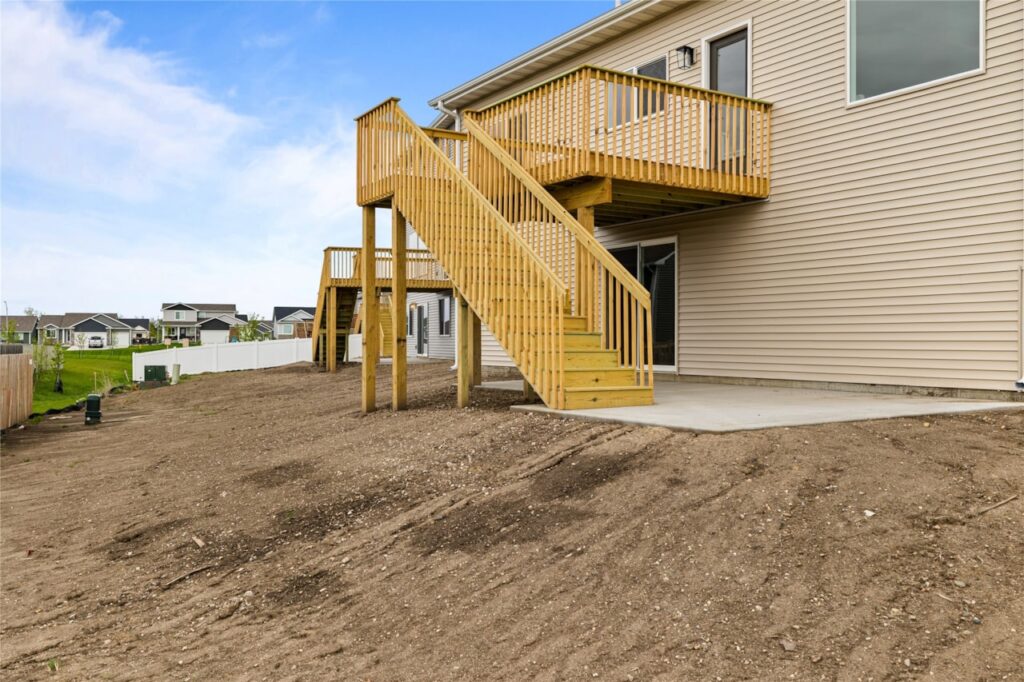 Rear exterior of new construction home with elevated wood deck, staircase, walkout basement slider, and backyard in Waukee Iowa