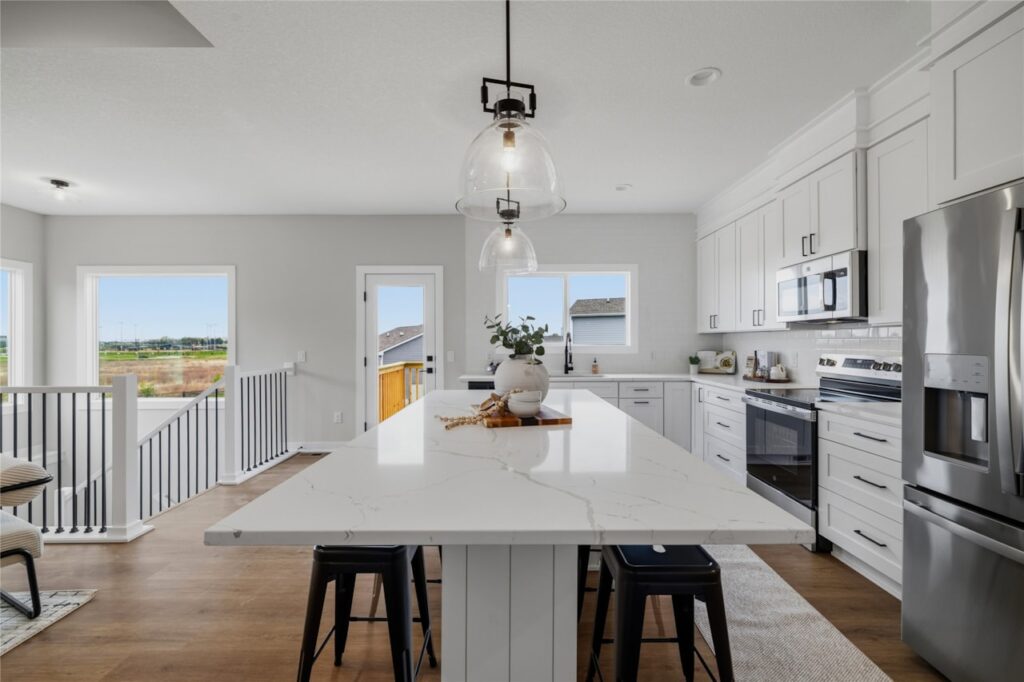 Kitchen island with quartz countertop, black bar stools, pendant light, and view to back deck in Waukee Iowa new construction