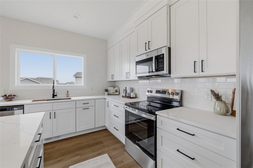 White shaker kitchen cabinets with stainless range, microwave, subway tile backsplash, and matte black sink in Waukee Iowa new build