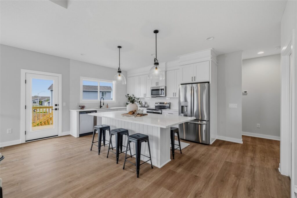 Open concept kitchen with shiplap island, four black bar stools, glass pendant lights, and back door in Waukee Iowa new construction