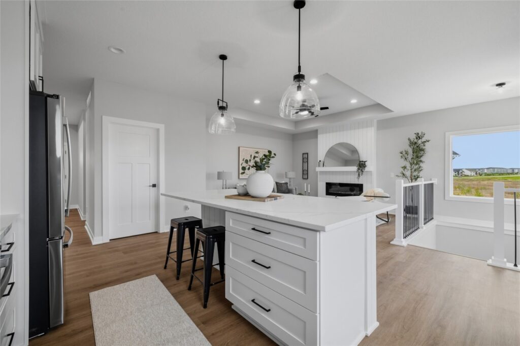 Open concept kitchen island with view to shiplap fireplace living room and tray ceiling in Waukee Iowa new home