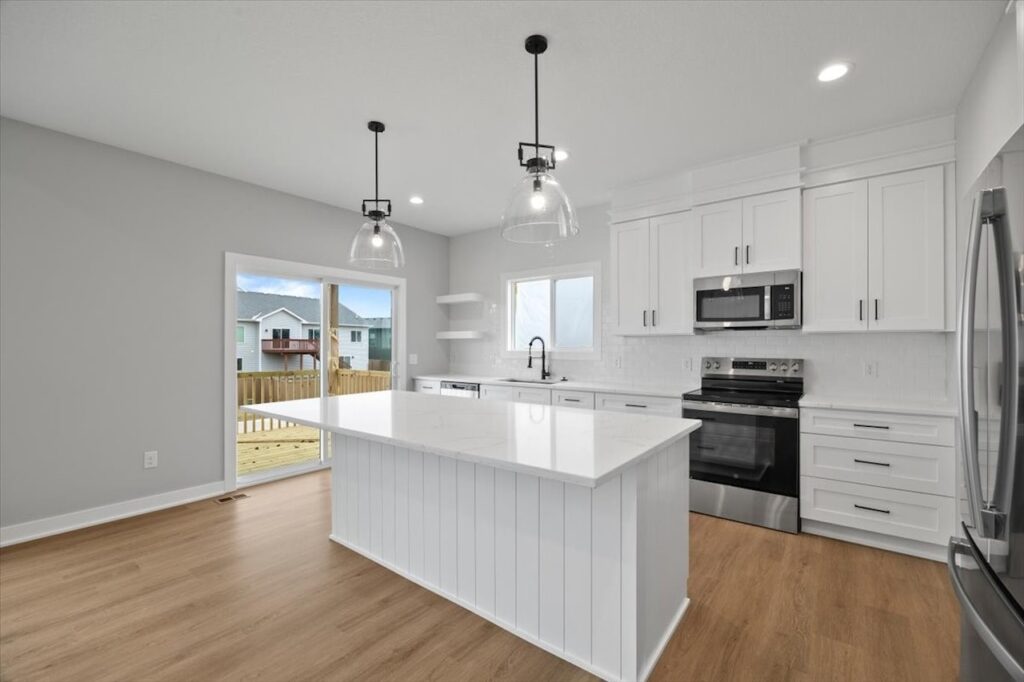 Modern white kitchen with stainless steel appliances and hardwood flooring, highlighting available homes at 321 11th St NW, Bondurant, IA.
