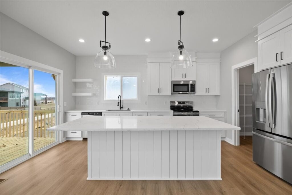 Sleek white kitchen with stainless steel appliances and hardwood floors, part of homes for sale at 321 11th St NW, Bondurant, IA.