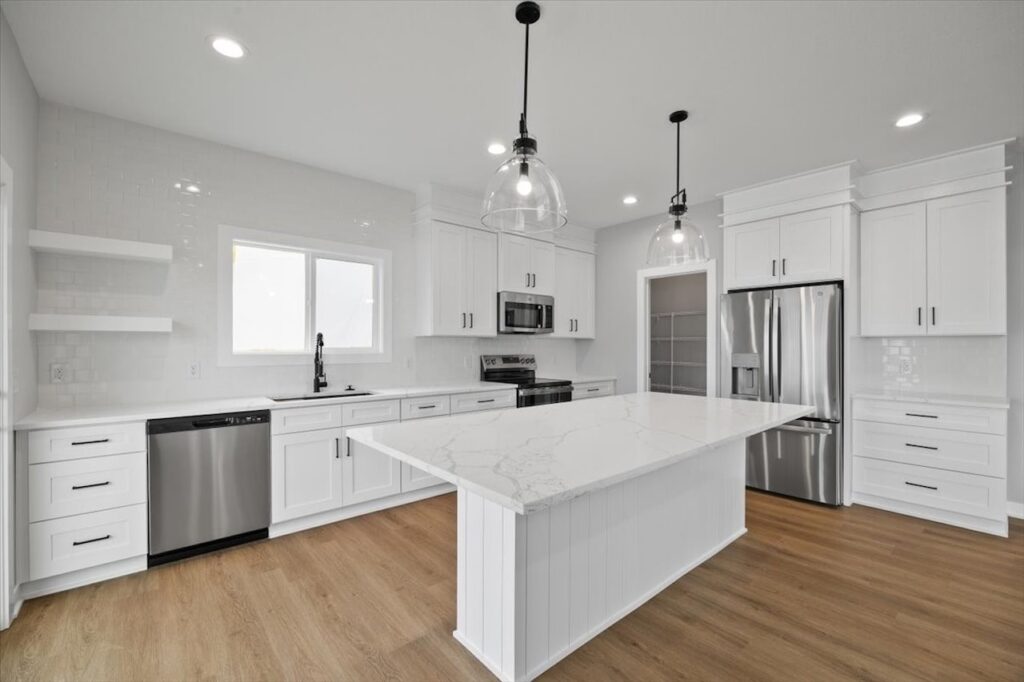 Bright white kitchen featuring stainless steel appliances and hardwood floors, showcasing homes for sale at 321 11th St NW, Bondurant, IA.