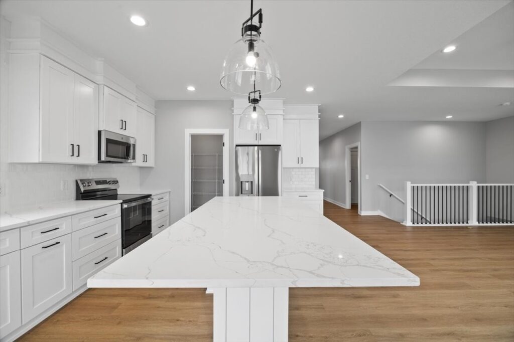 Bright white kitchen featuring stainless steel appliances and hardwood floors, showcasing homes for sale at 321 11th St NW, Bondurant, IA.