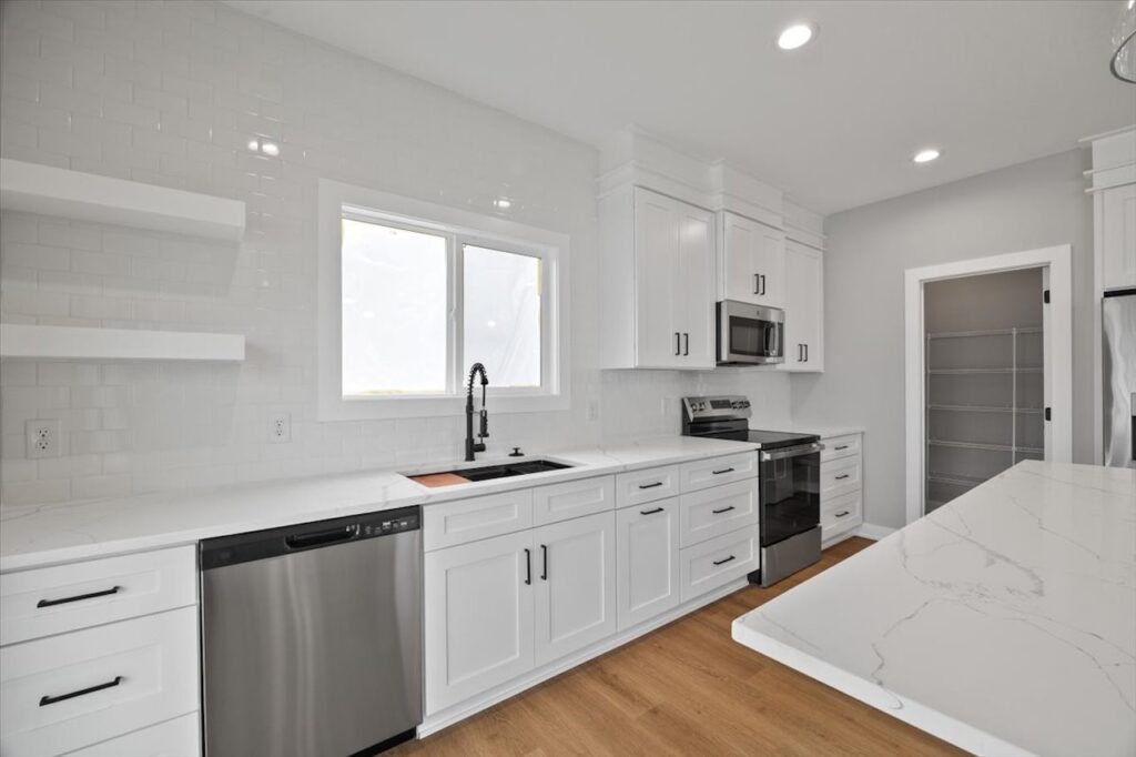 Bright white kitchen featuring stainless steel appliances, showcasing the available home for sale at 321 11th St NW, Bondurant, IA.