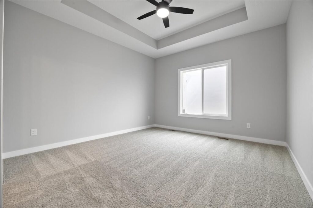 Empty room featuring carpet and a ceiling fan, part of available homes for sale at 321 11th St NW, Bondurant, IA.