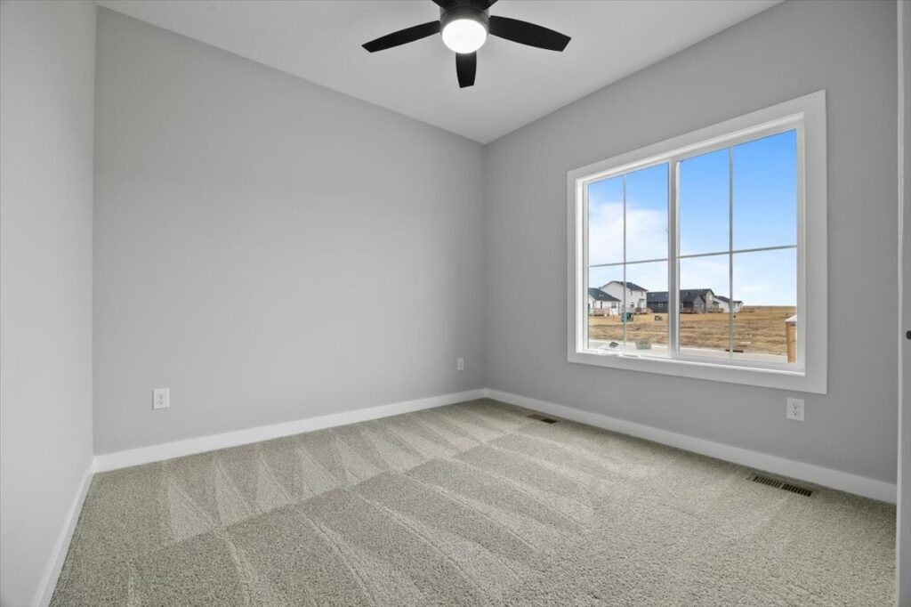 Empty room with carpet and ceiling fan, showcasing available homes for sale at 321 11th St NW, Bondurant, IA.