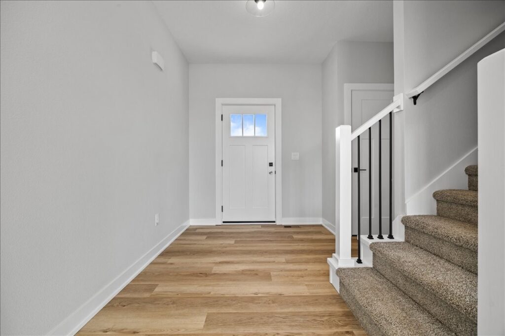 Hallway featuring a white door and wooden floors, part of a home for sale at 675 NW Rosemont Dr, Waukee, IA.