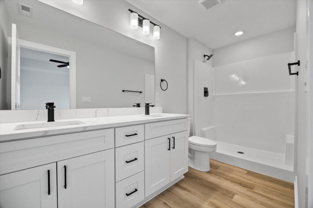 Clean white bathroom showcasing a toilet, sink, and shower, located in the home for sale at 675 NW Rosemont Dr, Waukee, IA.
