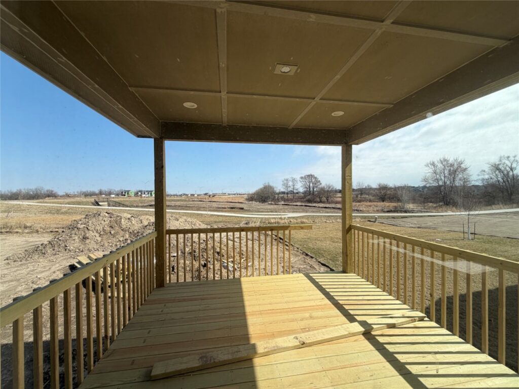 Covered wooden backyard deck overlooking open residential lots and scenic suburban landscape at new Gladiator Homes property for sale in Waukee, Iowa at 665 NW Rosemont Dr Waukee IA