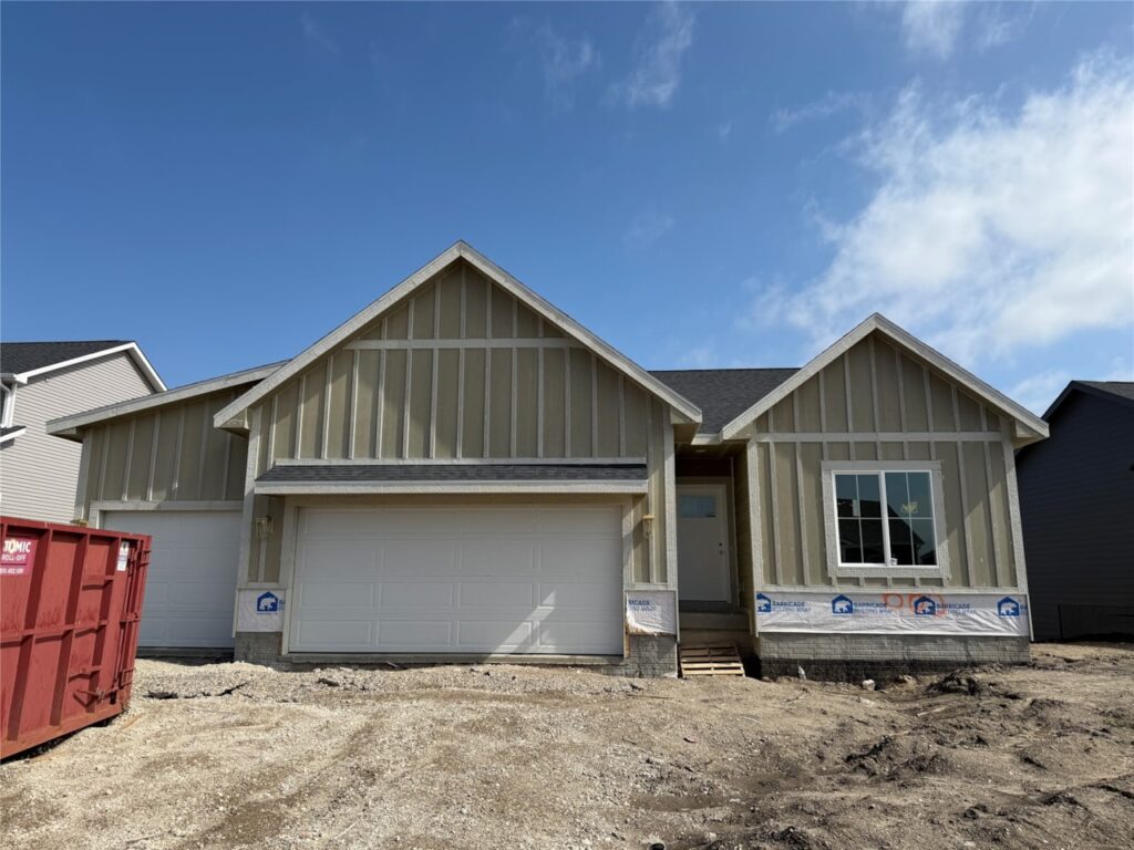A newly constructed single-story house in Waukee with a three-car garage, unfinished exterior siding, and a dirt front yard under a partly cloudy sky—one of the available homes for sale by Gladiator Homes at 665 NW Rosemont Dr, IA 50263.