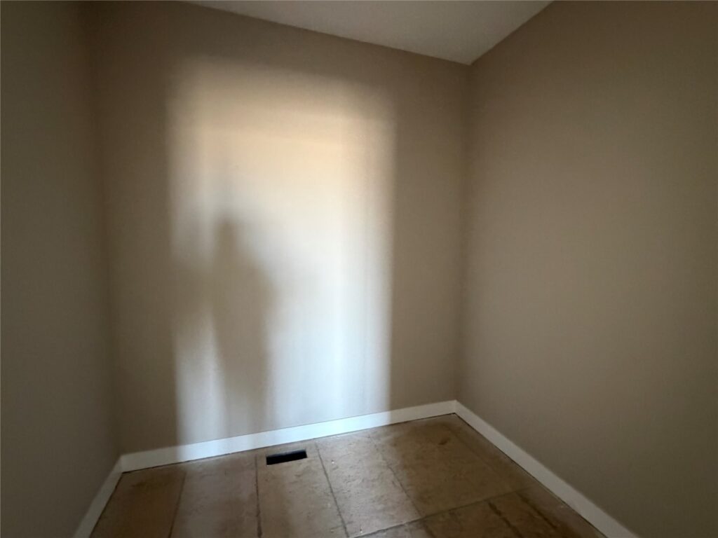 Empty beige room with bare plywood floor and a soft shadow of a person on the wall.