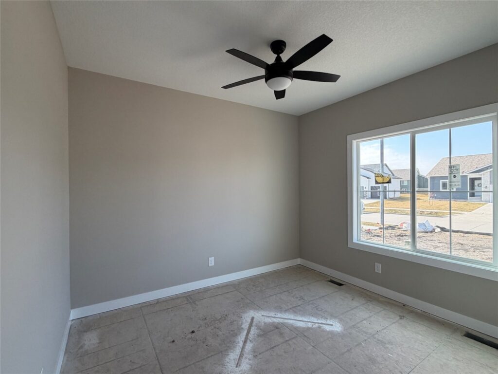 Empty modern living room under construction with a white fireplace, large windows, a ceiling fan, and a bare concrete floor.