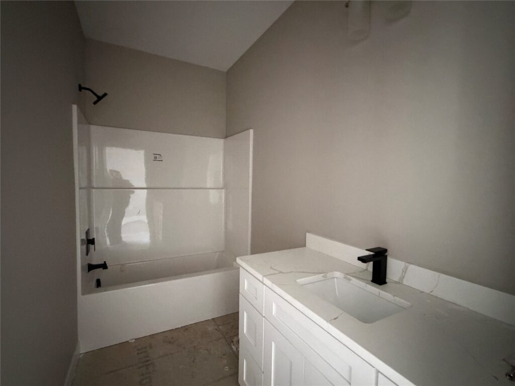 Minimalist bathroom with white bathtub, black fixtures, white vanity with marble countertop, and beige walls.