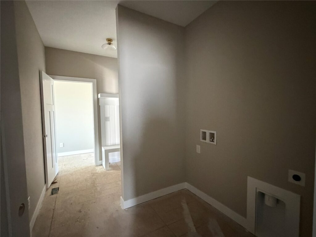 Unfinished laundry room with hookups on the right wall, beige walls, and a view into an adjacent room with white trim and built-in shelving—one of the available homes for sale by Gladiator Homes at 665 NW Rosemont Dr, Waukee, IA 50263.