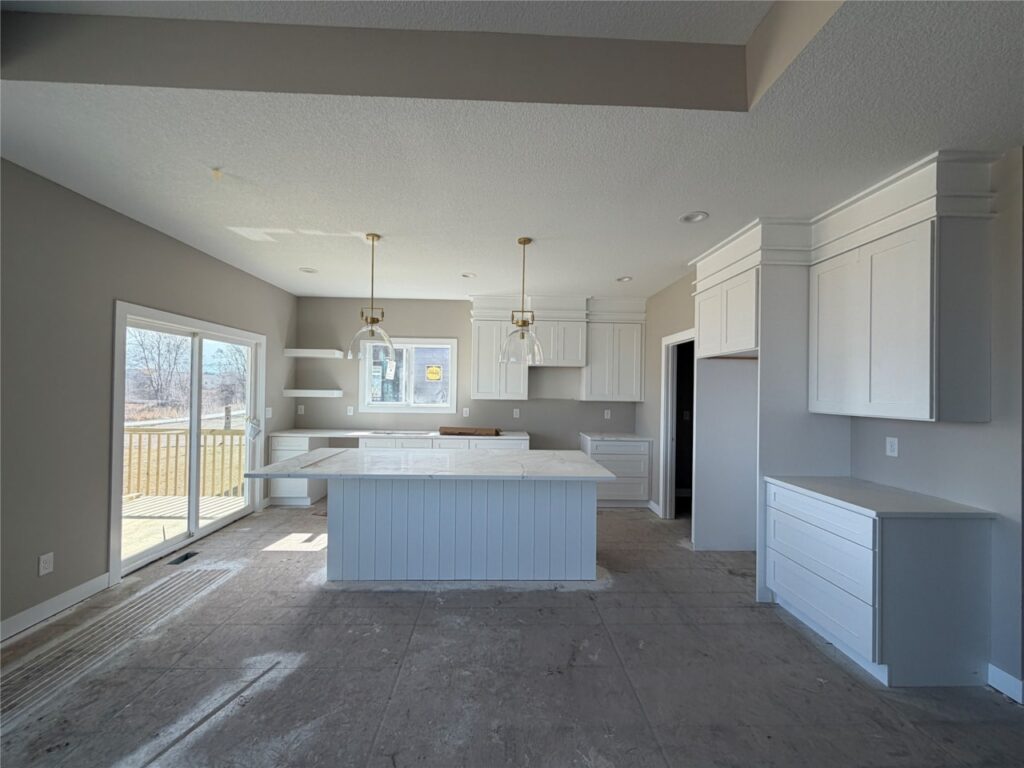 Modern open-concept kitchen with large white island, shaker cabinets, pendant lighting, and sliding glass doors in new Gladiator Homes property for sale at 665 NW Rosemont Dr, Waukee, Iowa.