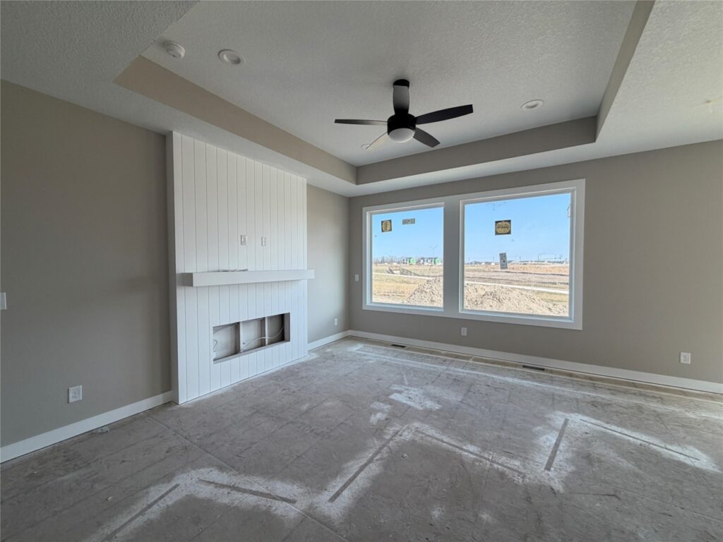 Empty modern living room under construction with a white fireplace, large windows, a ceiling fan, and a bare concrete floor.