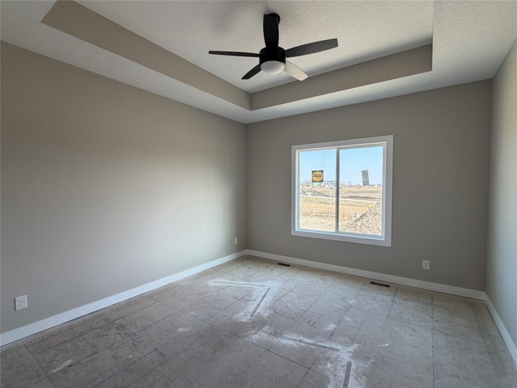 Empty room with beige walls, a ceiling fan, a window casting light on an unfinished floor and an open closet door.